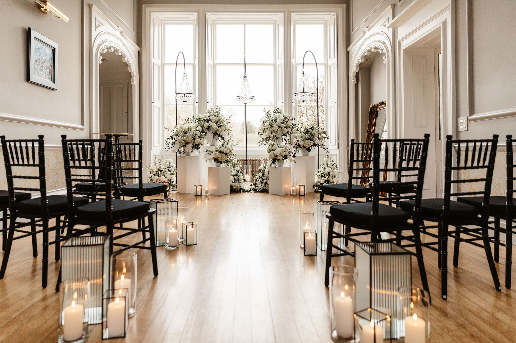 Indoor wedding ceremony setup at Netherbyres with black chairs, white floral pillars, and lantern candles styled by Ayrshire wedding florist and stylist.