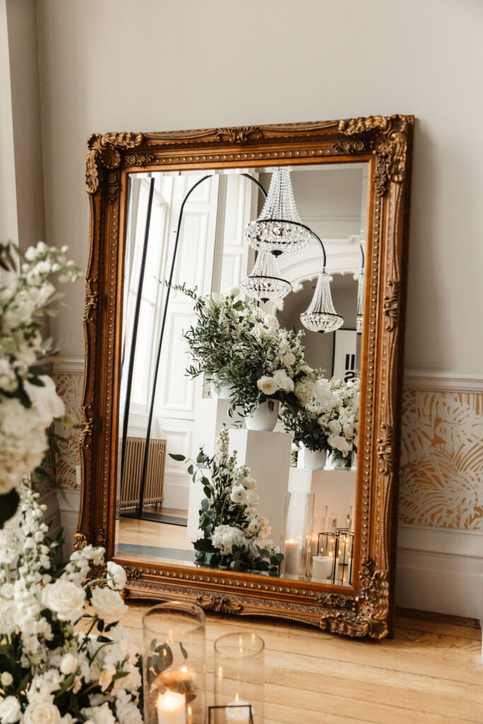 Elegant floral installation reflected in a gilt mirror at Netherbyres House with white roses and candles.