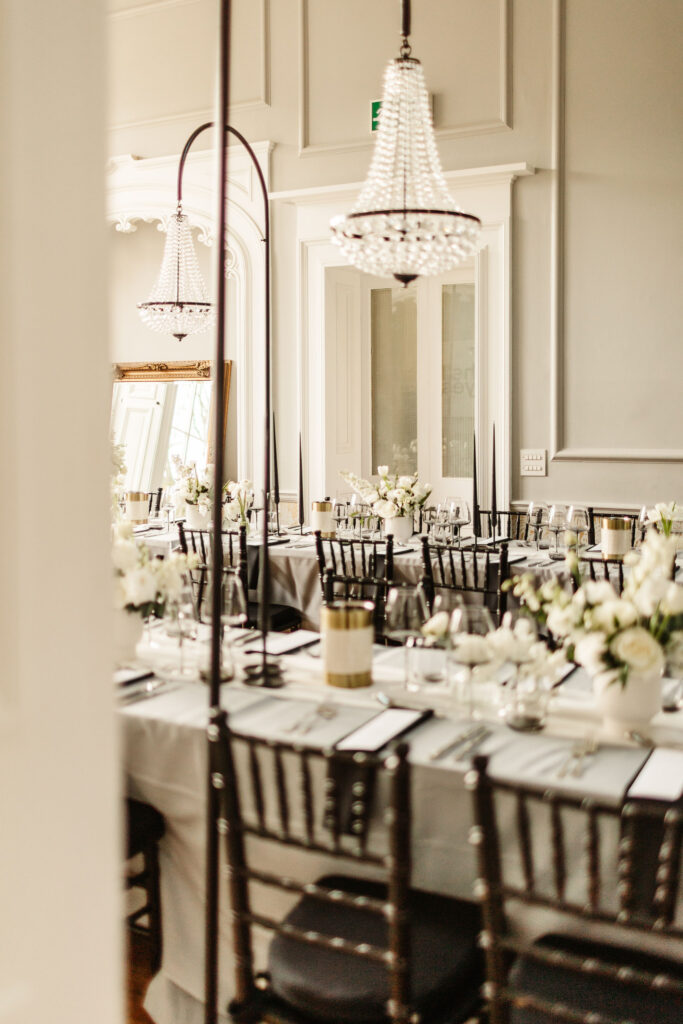 Elegant wedding reception setup with black chairs, white florals, and black taper candles under crystal chandeliers at Netherbyres House.