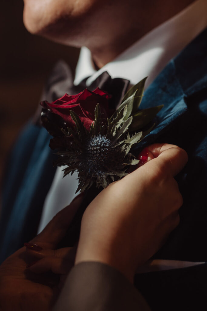 Close-up of groom’s boutonnière with red rose and blue thistle, styled by Paperwhite Floral Design for a wedding at Mount Stuart.